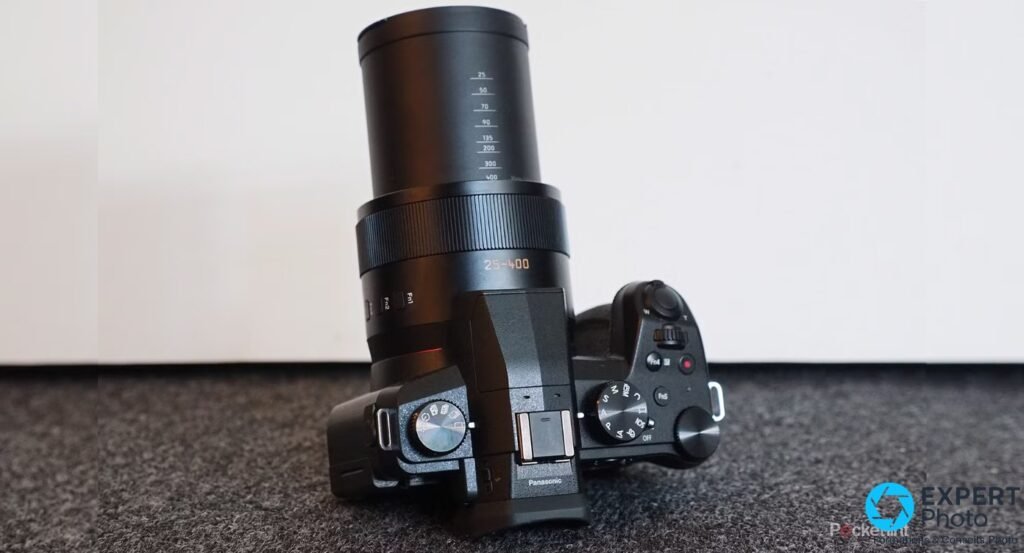  Panasonic Lumix FZ1000 II vue dessus, zoom étendu à 400 mm, repères de focales 25 à 400 gravés, molette de modes et bouton vidéo rouge visibles 