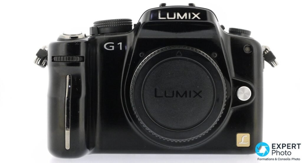 Panasonic Lumix G1 vu de face, cache d'objectif LUMIX monté sur la monture micro 4/3, fond studio blanc uni.