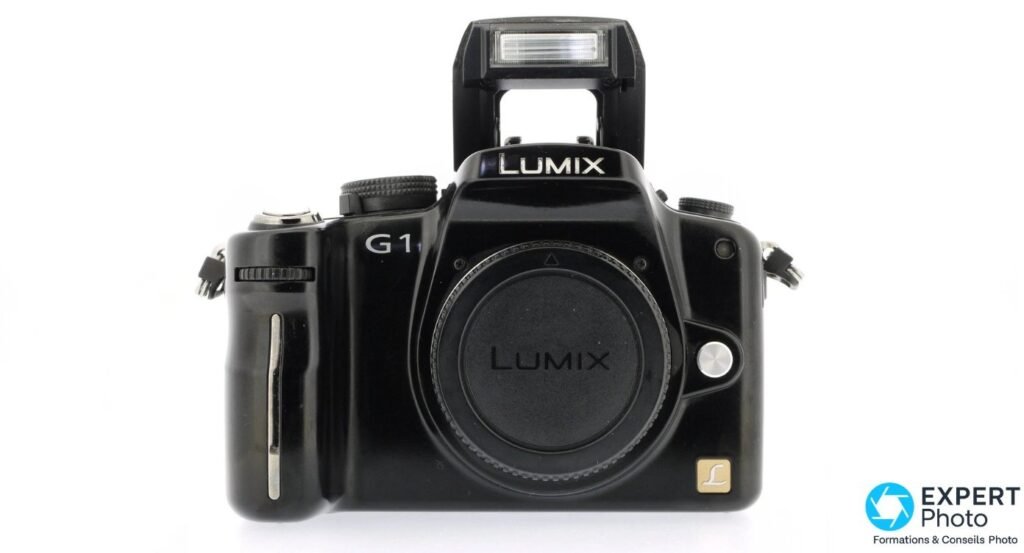 Panasonic Lumix G1 de face, flash pop-up sorti et cache d'objectif LUMIX en place, vue studio fond blanc. 