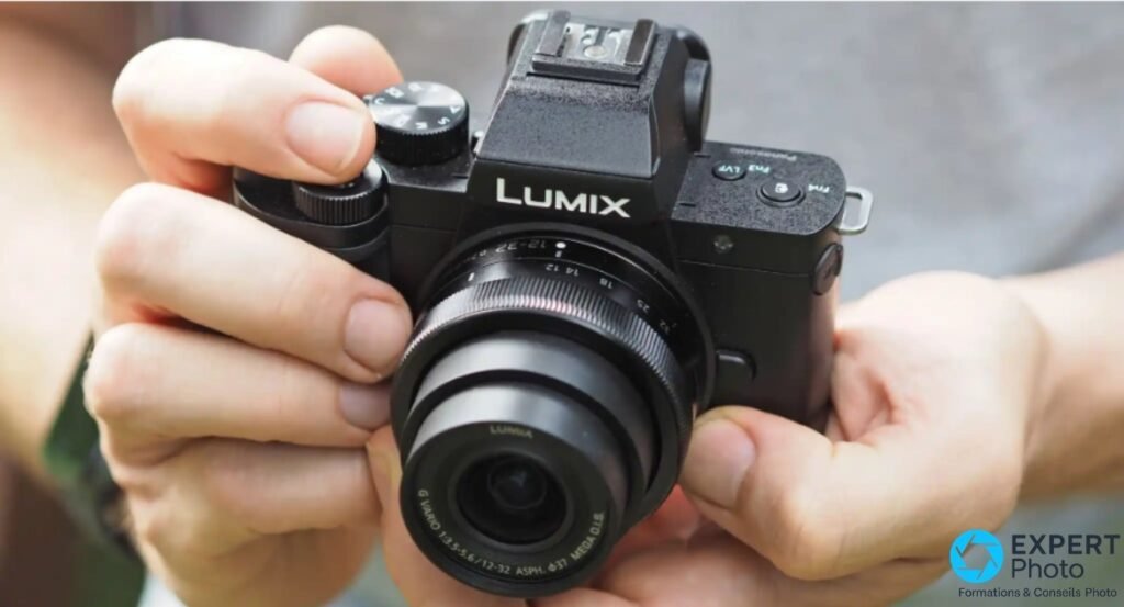 Panasonic Lumix G110 / G100 tenu à deux mains face caméra, illustre la prise en main compacte avec son objectif 12-32 mm.