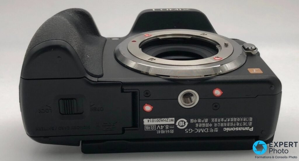 Vue de dessous du Panasonic Lumix G5 avec marquage DMC-G5, trappe Memory Card/Battery, verrou Lock/Open et filetage trépied. 
