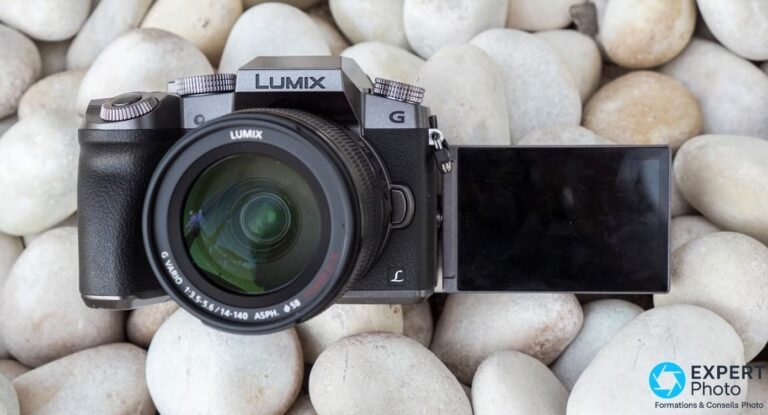 Panasonic Lumix G7 : avis, prix occasion et vrai verdict en 2026 Panasonic Lumix G7 bi-ton vu de 3/4 avant, écran LCD orientable déplié, objectif Lumix 14-140 OIS sur fond de galets clairs.