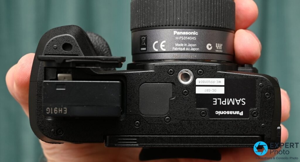 Dessous du Panasonic Lumix G97 : pas de vis trépied 1/4, trappe batterie et référence objectif H-FS014045 