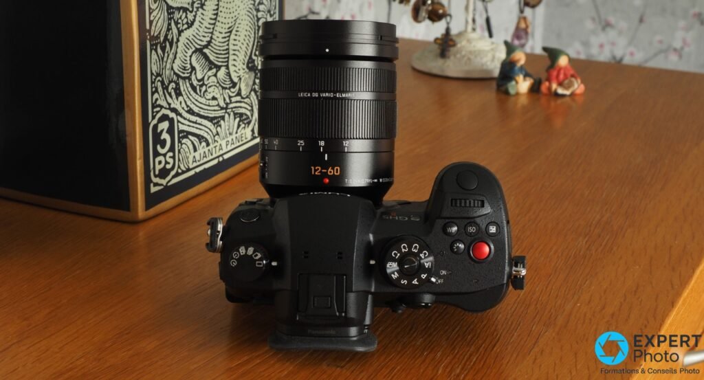 Panasonic GH5 II vu du dessus avec objectif Leica DG Vario-Elmarit 12-60 mm monté, bouton rouge et molette de modes visibles 