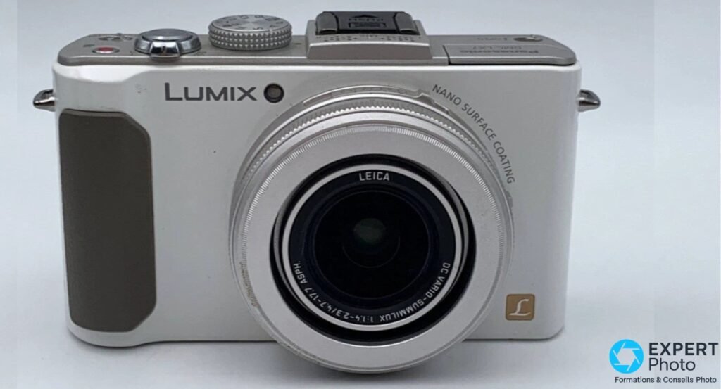Panasonic Lumix DMC-LX7 blanc vu strictement de face, exemplaire posé sur surface gris clair.