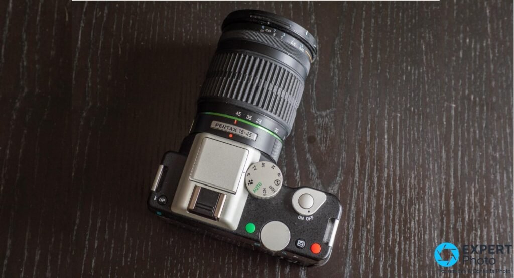 Pentax K-01 vue plongeante dessus avec zoom Pentax 16-45 mm monté, molette de modes AUTO/SCN et boutons ON/OFF visibles