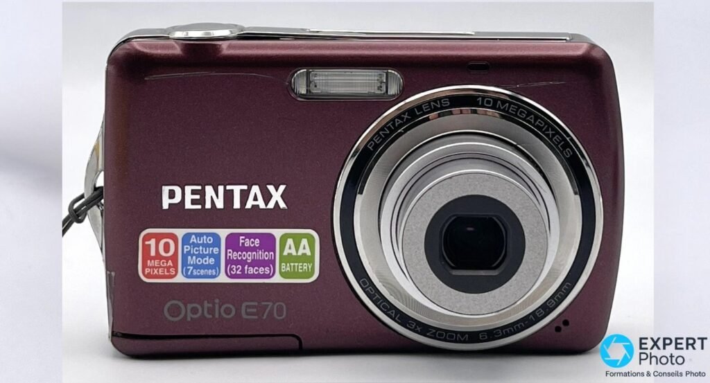 Pentax Optio E70 prune vu de face, objectif zoom 3x sorti, marquage Optical 3x Zoom 6.3-18.9mm lisible.