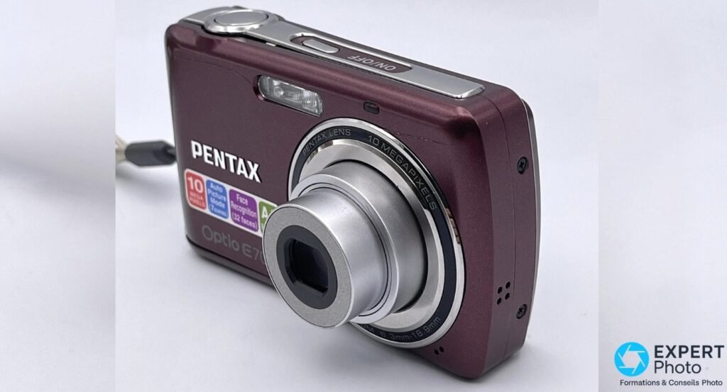  Pentax Optio E70 prune en marche, objectif zoom déployé, bouton ON/OFF gravé visible sur le dessus.