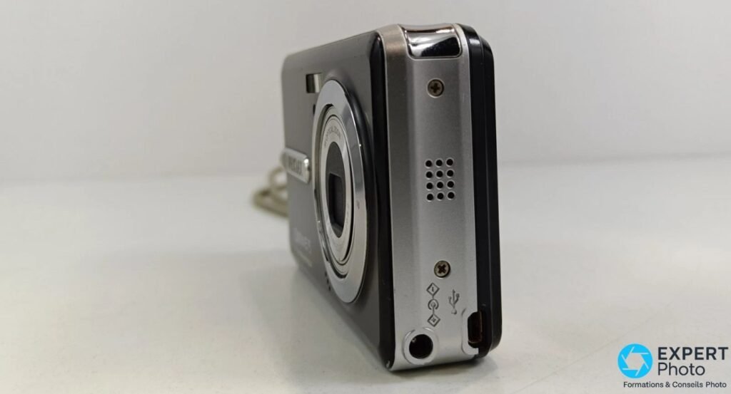 Trois quarts arrière du Pentax Optio E75, port USB propriétaire, haut-parleur perforé et pictogrammes connecteurs.