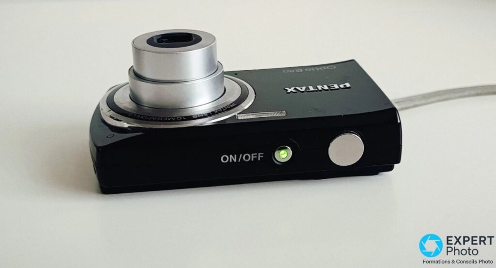 Pentax Optio E80 noir vu de dessus, objectif déployé, déclencheur métallique et LED verte de mise sous tension allumée. 