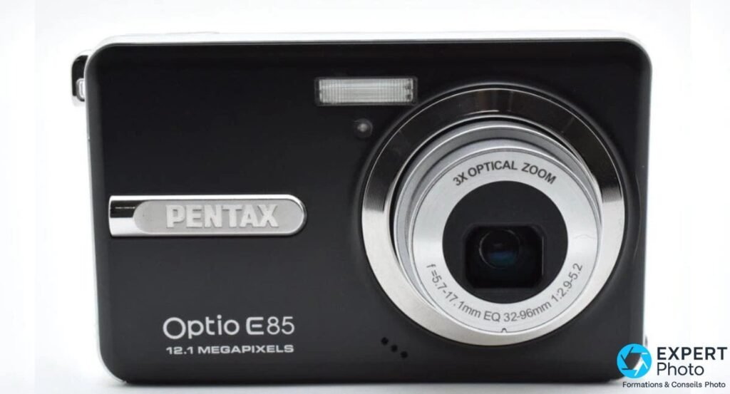 Pentax Optio E85 noir vu de face, logo PENTAX, Optio E85 12.1 Megapixels et objectif 3X OPTICAL ZOOM déployé visible.
