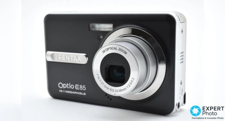 Avis Pentax Optio E85 : ce que vaut ce compact CCD vintage Pentax Optio E85 noir vu de trois quarts avant gauche, logo PENTAX argenté, objectif 3X OPTICAL ZOOM déployé à droite.