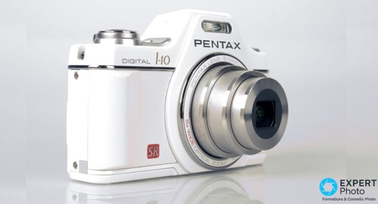 Pentax Optio I-10 : avis 2026 et guide d’achat occasion du compact CCD inspiré du Pentax Auto 110 Pentax Optio I-10 blanc en trois quarts avant, objectif zoom 5x déployé, design reflex miniature visible.