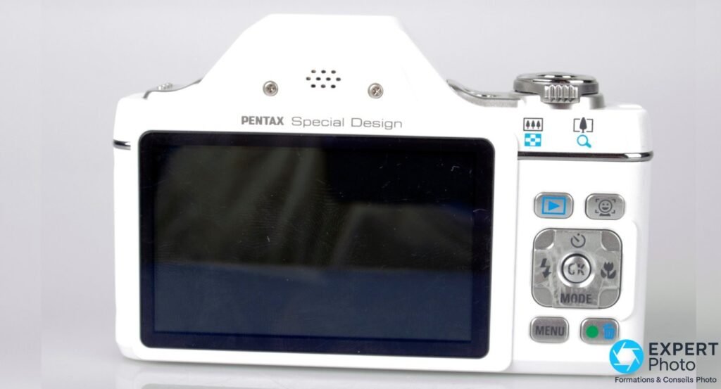 Pentax Optio I-10 blanc vu de dos, écran LCD 2,7 pouces, pavé directionnel et boutons MENU et OK visibles.