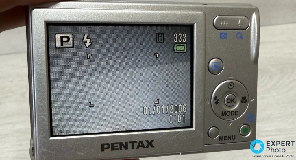Pentax Optio M10 tenu en main, écran LCD allumé en mode P, indicateur 333 photos restantes et date 01/01/2006.