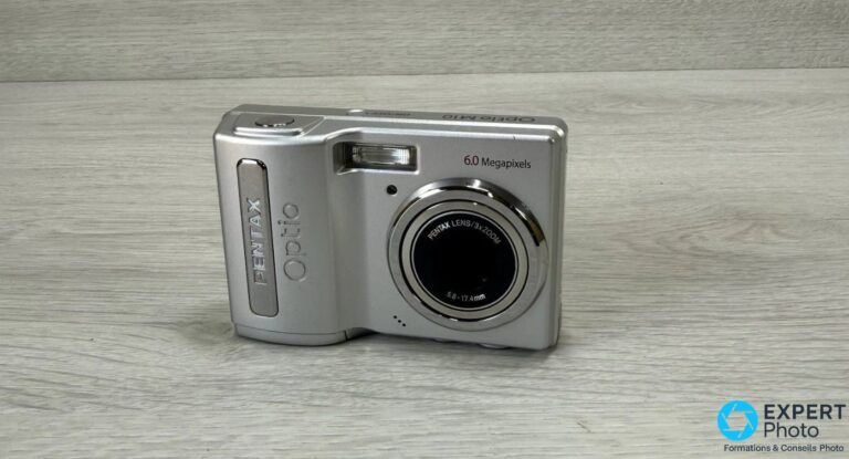 Pentax Optio M10 : avis honnête et guide d’achat occasion en 2026 Pentax Optio M10 vu de face en trois-quarts, boîtier argenté avec marquages 6.0 Megapixels et PENTAX LENS 3X ZOOM.