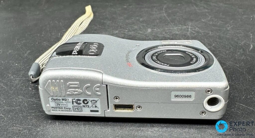 Pentax Optio M20 vue de dessous : port USB ouvert et étiquette technique Pentax Corp.
