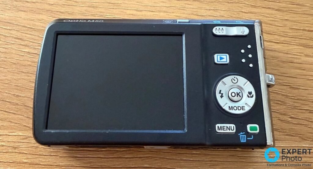 Pentax Optio M50 vu de l'arrière, écran LCD 2,5 pouces éteint, molette OK/MODE, boutons MENU et lecture. 