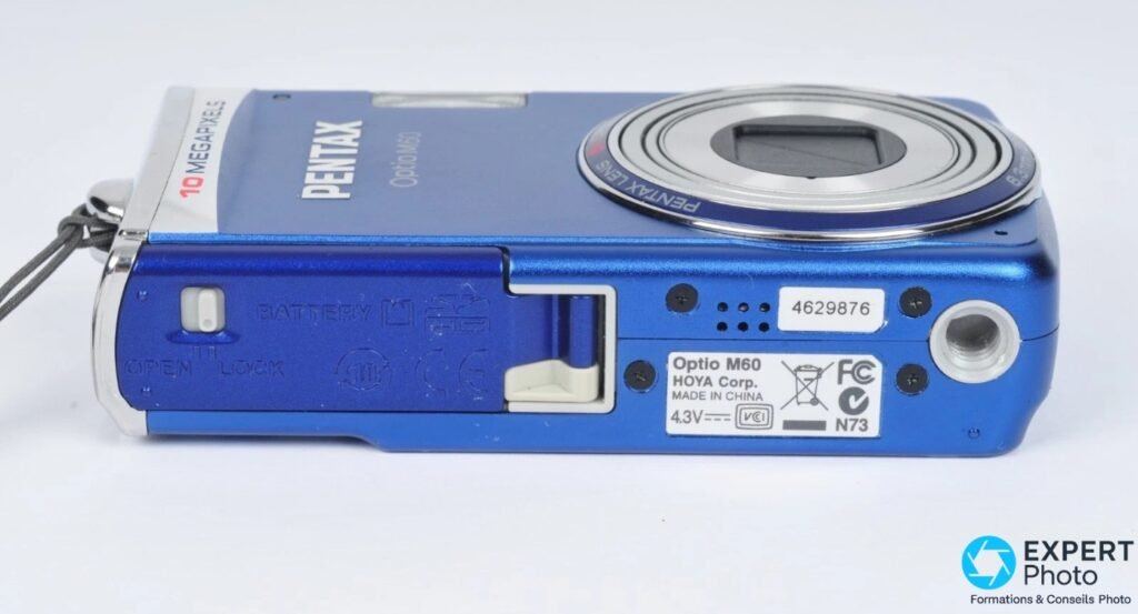 Pentax Optio M60 bleu, dessous, trappe batterie ouverte, étiquette Hoya Corp. 4.3V, pas de filetage trépied visible 
