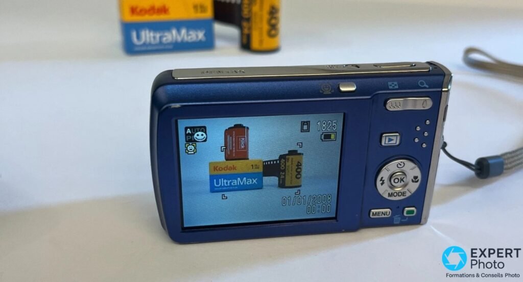 Pentax Optio M60 bleu, écran allumé affichant un viseur live, boîte Kodak UltraMax en arrière-plan hors netteté