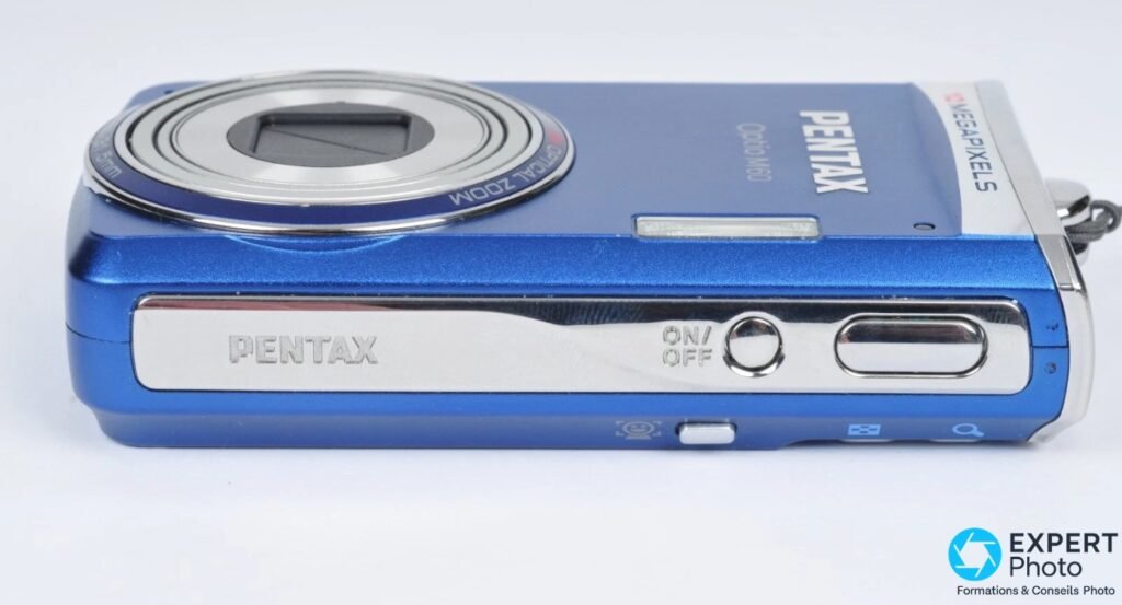 Pentax Optio M60 bleu, tranche supérieure, bouton ON/OFF et déclencheur argentés, bague objectif visible en arrière