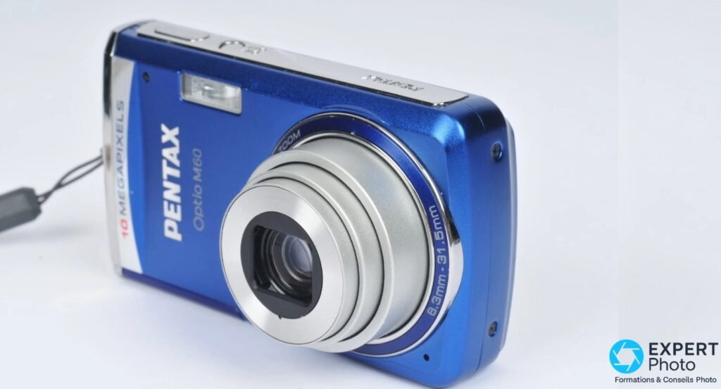 Pentax Optio M60 bleu, vue plongée 3/4 avant-droit, bague objectif gravée 6,3–31,5 mm, flash visible 