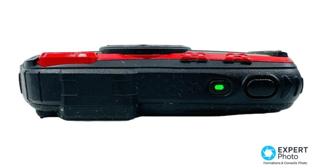 Tranche supérieure du Pentax WG-10 rouge et noir, voyant LED vert allumé et deux boutons circulaires noirs visibles