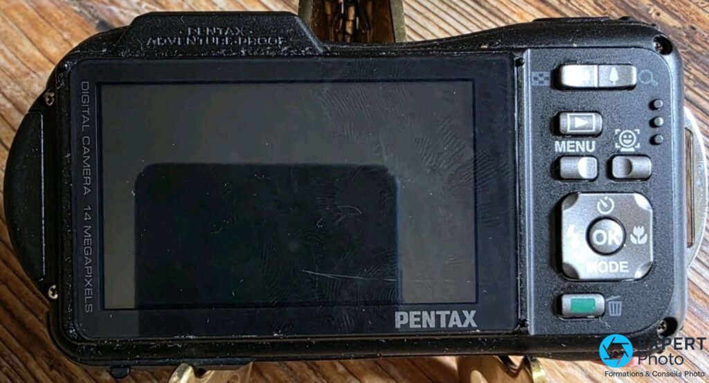 Face arrière du Pentax WG-10, grand écran LCD éteint avec rayures visibles, boutons MENU, OK, MODE et molette de navigation
