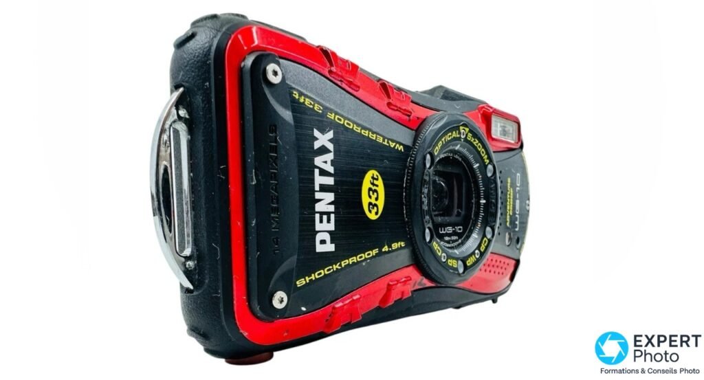 Pentax WG-10 rouge et noir en vue 3/4 avant gauche, volet de connecteur circulaire chromé sur la tranche, inscriptions Waterproof et Shockproof