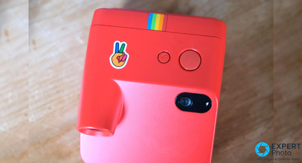 Polaroid Go Gen 2 rouge vu de dessus avec deux boutons ronds, bloc commande oval et sticker peace collé sur le boîtier 