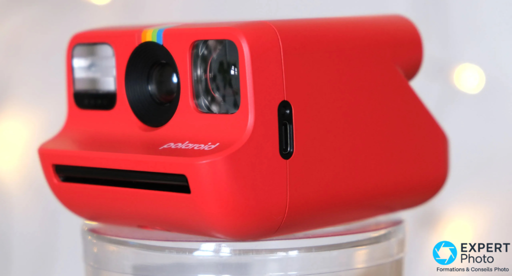  Polaroid Go Gen 2 rouge en vue 3/4 avant sur support transparent, fente d'éjection et port USB-C visibles