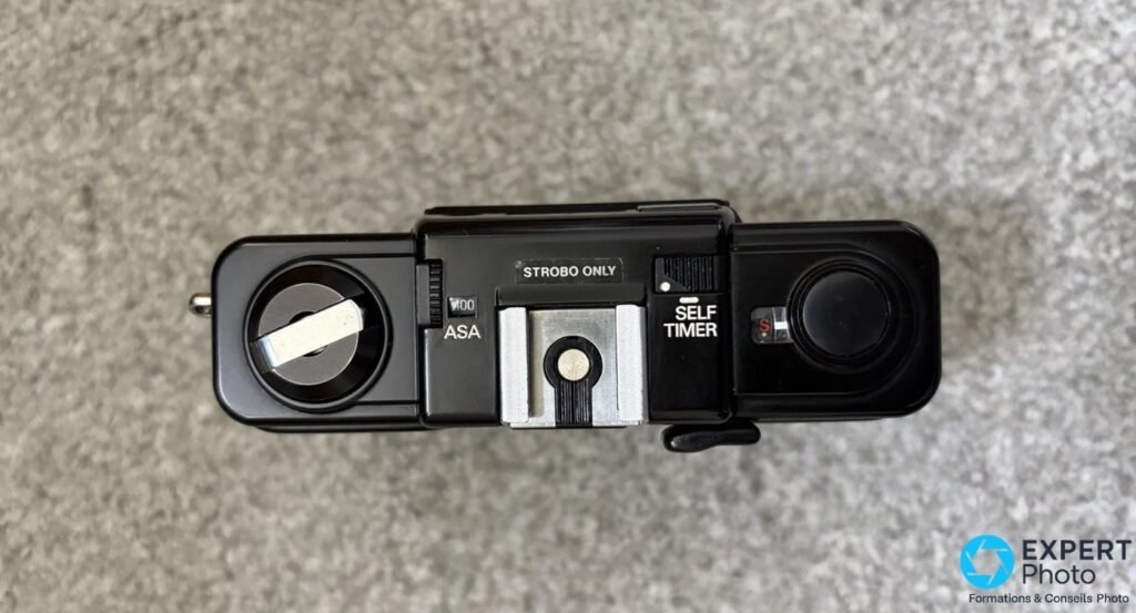 Dessus du Ricoh FF-1S : molette ASA, repère STROBO ONLY, griffe flash, sélecteur SELF TIMER, déclencheur et manivelle