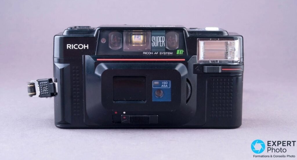 Ricoh FF-3 AF Super noir vu de face, cache d'objectif noir clipsé devant l'optique, fenêtre ISO ASA visible. 