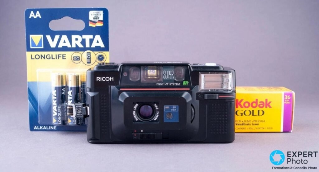 Ricoh FF-3 AF Super avec un blister de piles AA Varta Longlife à gauche et un film Kodak Gold 36 poses à droite.