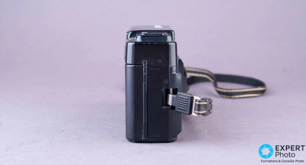 Ricoh FF-3 AF Super vu de profil gauche, attache de dragonne métallique avec sangle noire à bandes pendante. 