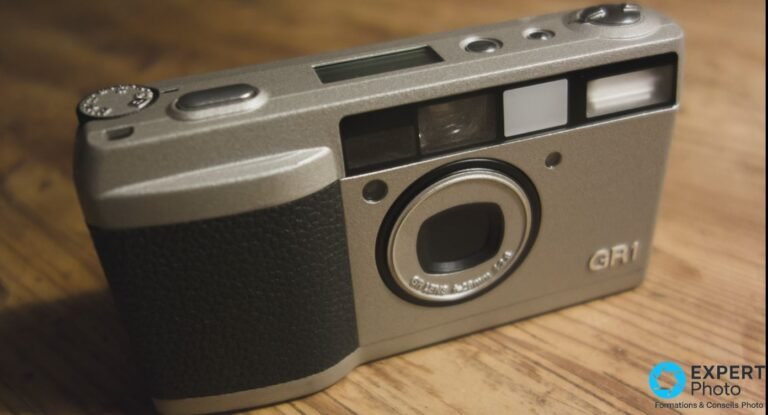 Ricoh GR1 argentique gris champagne en vue trois-quarts avant, marquage GR1 lisible, posé sur table en bois.