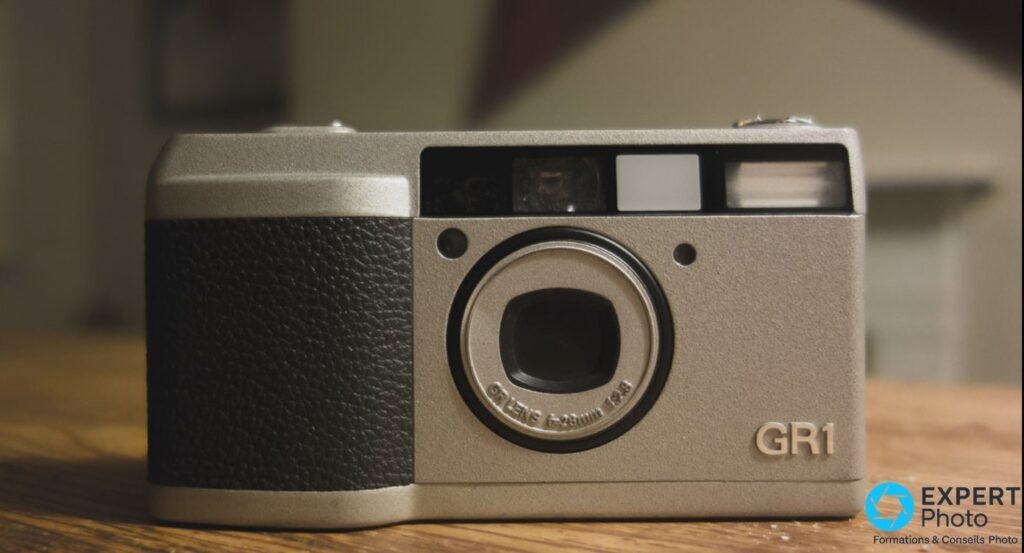 Ricoh GR1 argentique gris champagne en vue strictement frontale, gravure GR LENS 28 mm et marquage GR1.