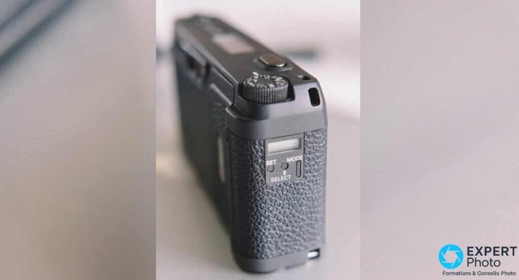 Ricoh GR1v vu de l'arriere en perspective, boutons SET, MODE et SELECT visibles sur la face dorsale.
