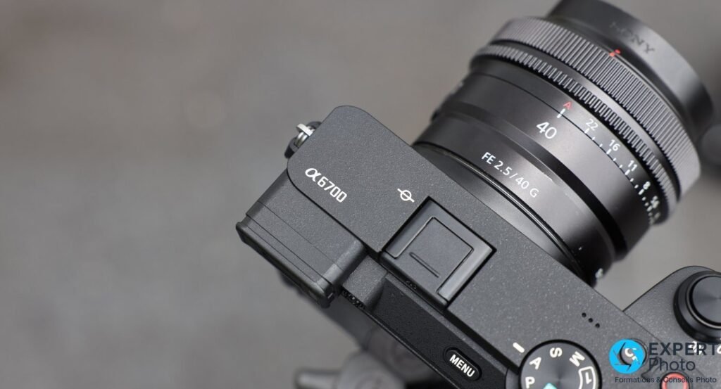 Détail du dessus du Sony A6700 : logo α6700 gravé, griffe porte-flash et amorce de l'objectif FE 2.5/40 G.