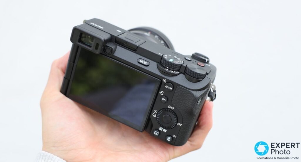Sony A6700 tenu en main, vue arrière, écran orientable et boutons MENU, AF-ON, Fn, DISP, ISO, C3 visibles.