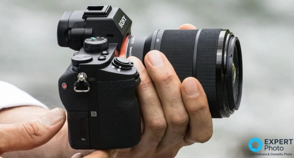 Sony Alpha 7 II tenu en main droite, profil gauche, équipé d'un zoom FE 28-70 mm OSS réglé à 50 mm, logo NFC visible.