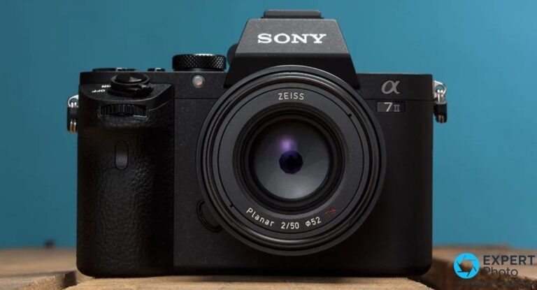 Sony Alpha 7 II de face avec objectif Zeiss Planar 2/50 Φ52 T*, marquage α 7 II lisible, fond bleu uni.