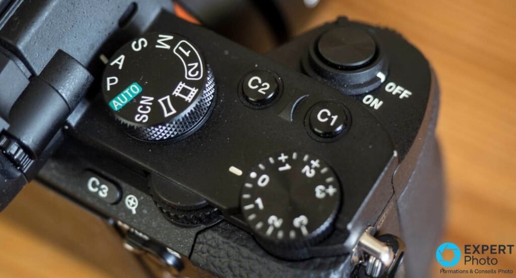 Plaque supérieure d'un Sony Alpha 7 II : molette de mode sur AUTO, boutons C1 et C2, molette de compensation d'exposition sur 0.