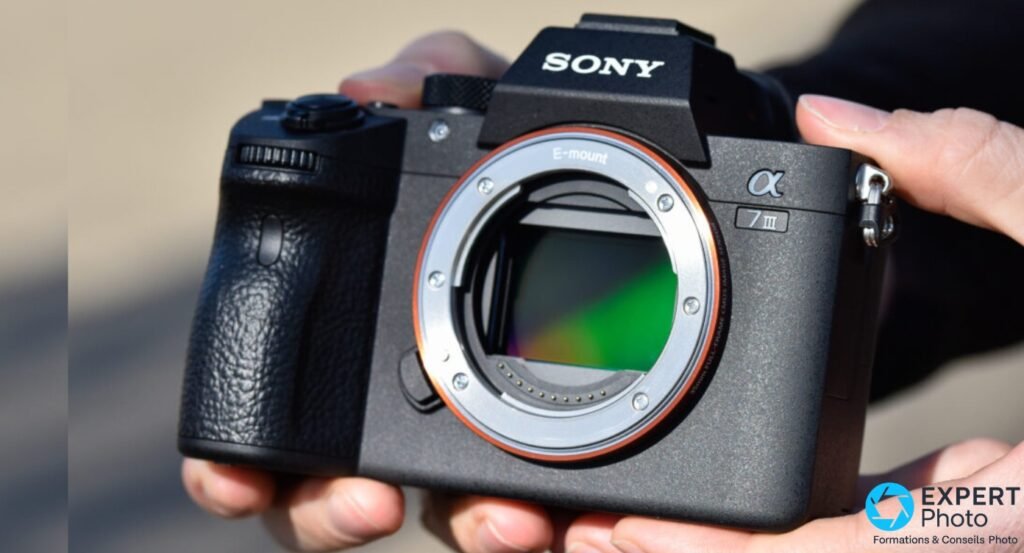 Sony A7 III boîtier nu, monture E-mount argentée avec bague orange, capteur BSI plein format visible, tenu des deux mains