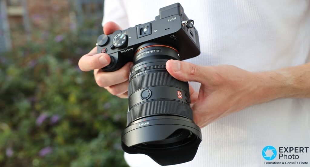  Sony A7C II tenu à deux mains avec objectif Sony FE 16-35 mm f/2.8 GM II monté, en extérieur sur fond flou 