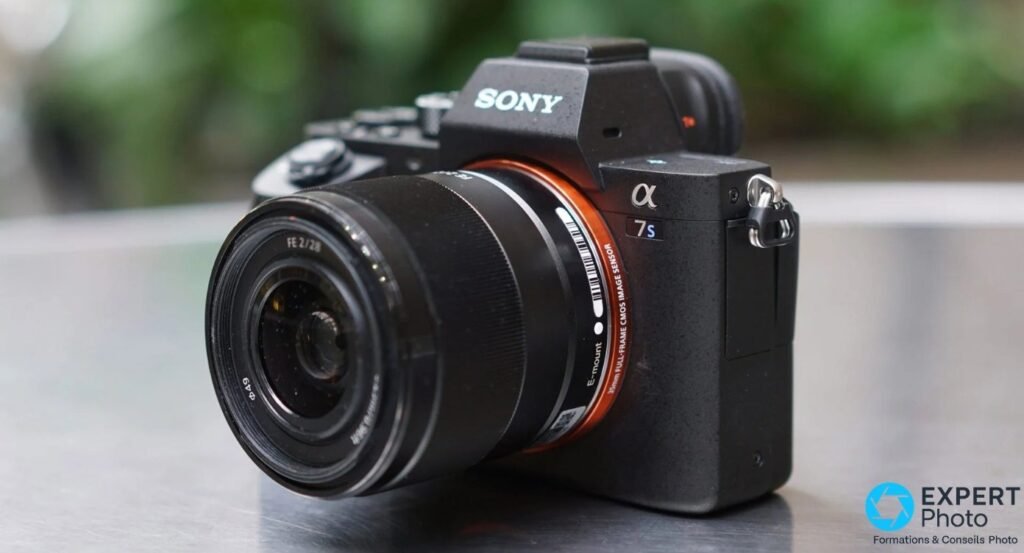 Sony A7S II avec objectif Sony FE 28mm f/2, vue 3/4 avant sur surface métallique, fond végétal flou.