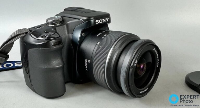 Sony Alpha 100 (DSLR-A100) : avis détaillé du premier reflex Sony en 2026 Sony Alpha 100 (DSLR-A100) en vue trois quarts droite avec objectif Sony DT 18-55 mm f/3.5-5.6 SAM monté.