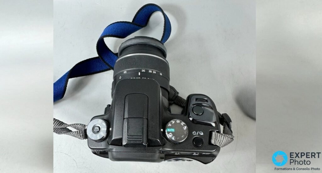 Vue de dessus du Sony Alpha 100 avec molette des modes sur AUTO, déclencheur et objectif 18-55 mm SAM à l'échelle de focales.