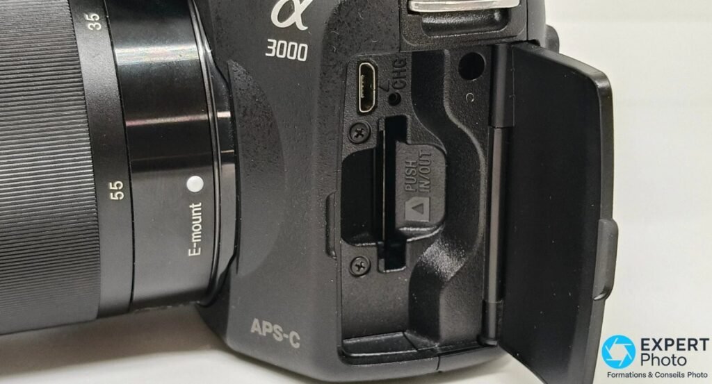 Ports latéraux du Sony Alpha 3000 ouverts : prise micro-USB CHG, prise jack et fente de carte mémoire PUSH IN/OUT. 