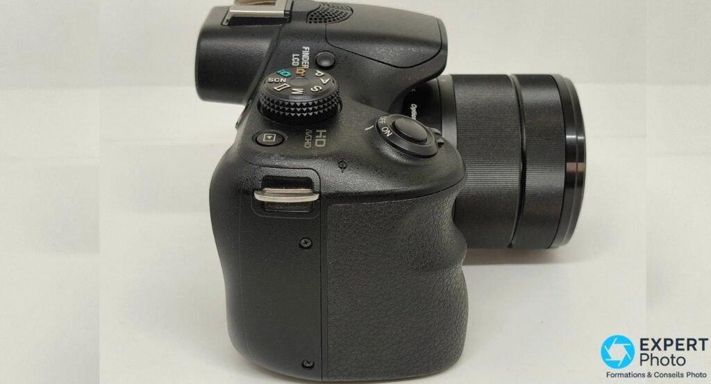 Détail du côté droit du Sony Alpha 3000 avec bouton FINDER/LCD, molette de modes et marquage HD AVCHD gravé sur le boîtier. 